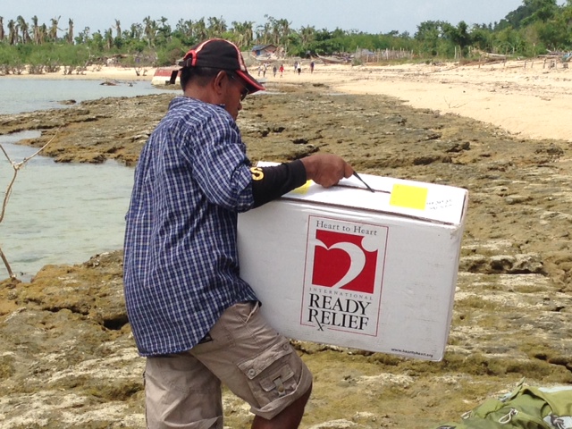 A Filipino man carries a HHI Ready Relief Box onto a beach on Isla Gigantes, Philippines, after offloading it from a boat.